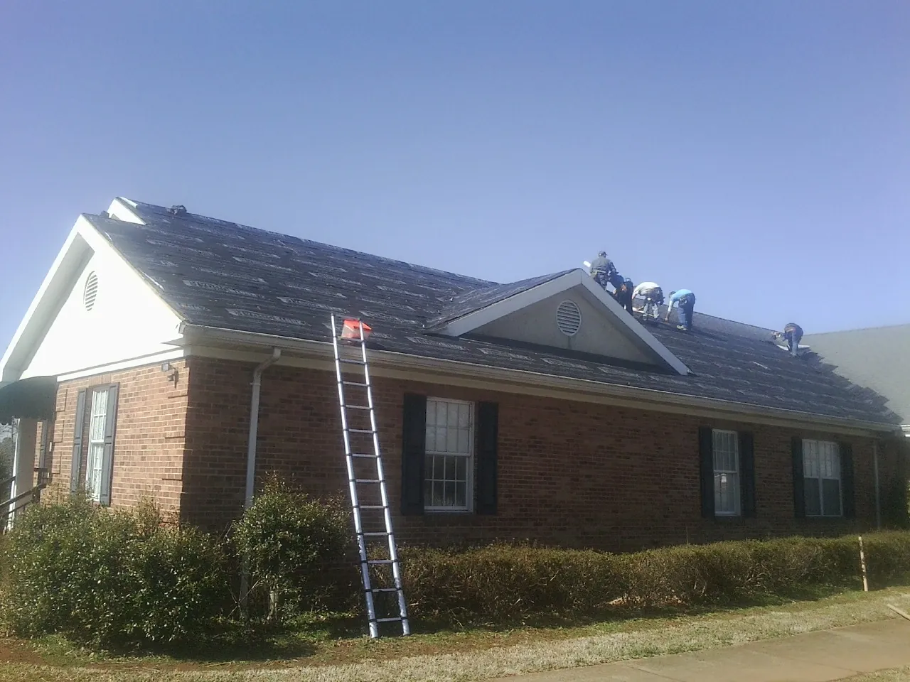 Crew tearing shingles off a brick ranch roof with a ladder set — Metal Roof Repair work by our crew in Charleston